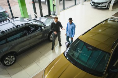 Erkek müşterinin portresi galeride profesyonel araba satıcısıyla konuşuyor. Yeni otomobil seçimi ve satın alma kavramı.