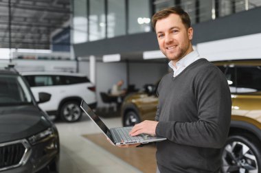 Araba satıcısı araba salonunda duruyor ve müşterilerin satışa çıkmasını bekliyor..