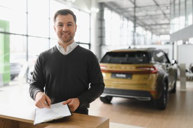 Araba satıcısı araba salonunda duruyor ve müşterilerin satışa çıkmasını bekliyor..