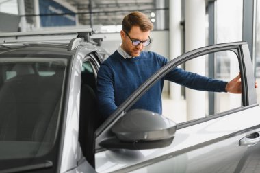 Genç adam yeni bir araç içinde araba Bayilik seçmektir.