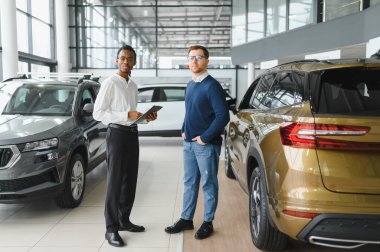 Erkek araba satıcısı araba galerisinde müşteriye araba seçmesinde yardımcı olur. Adam yeni araba alıyor..