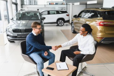 Araba galerisindeki yönetici araba satıcısı. Masada erkek alıcıyla sözleşme imzalıyor..