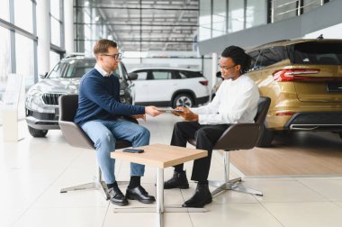 Araba galerisindeki yönetici araba satıcısı. Masada erkek alıcıyla sözleşme imzalıyor..