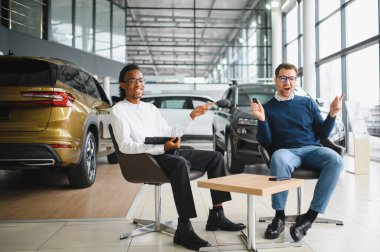 Araba galerisindeki bir masada bir müşteriyle oturan ve imzalamak için form veren bir satıcı. Almak, kiralamak ve bir arabayı sigortalamak..