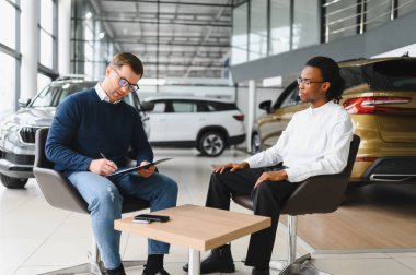Otomobil salonunda erkek müşteriyle anlaşma yapan bir satıcı. Araba merkezinden yeni araç alan sakallı adam..