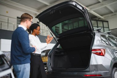 Erkek müşterinin portresi galeride profesyonel araba satıcısıyla konuşuyor. Yeni otomobil seçimi ve satın alma kavramı.