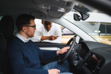 Erkek araba satıcısı araba galerisinde müşteriye araba seçmesinde yardımcı olur. Adam yeni araba alıyor..