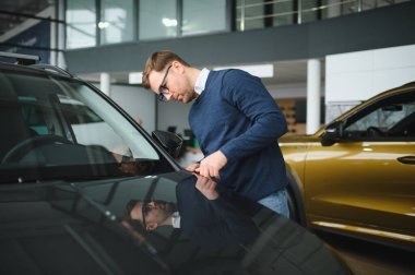 Genç adam yeni bir araç içinde araba Bayilik seçmektir.
