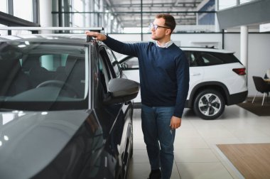 Genç adam yeni bir araç içinde araba Bayilik seçmektir.