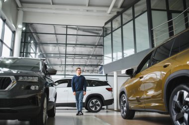 Genç adam yeni bir araç içinde araba Bayilik seçmektir.