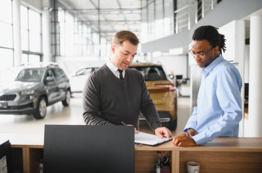Müşteri erkek, galeride otomobil satın alıyor, araba satıcısıyla kağıt imzalıyor. Galeride yeni otomobil alma kavramı.