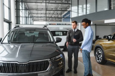 Erkek araba satıcısı, galeride dalgın genç bir müşteriyle sohbet ediyor. Satış merkezinden araba alırken adam dinliyor.