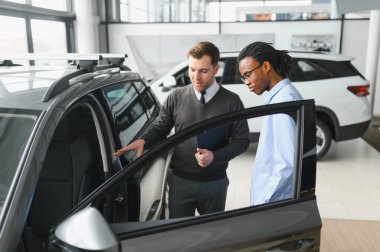 Erkek araba satıcısı, galeride dalgın genç bir müşteriyle sohbet ediyor. Satış merkezinden araba alırken adam dinliyor.