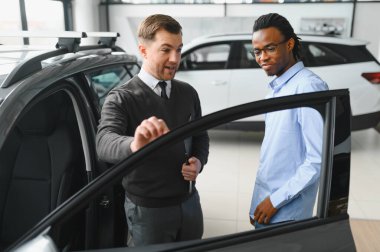 Erkek araba satıcısı, galeride dalgın genç bir müşteriyle sohbet ediyor. Satış merkezinden araba alırken adam dinliyor.