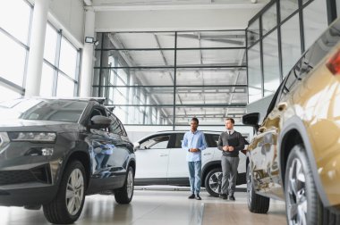 Erkek müşterinin portresi galeride profesyonel araba satıcısıyla konuşuyor. Yeni otomobil seçimi ve satın alma kavramı.