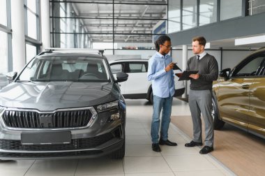 Erkek araba satıcısı araba galerisinde müşteriye araba seçmesinde yardımcı olur. Adam yeni araba alıyor..