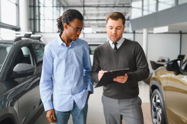 Erkek araba satıcısı araba galerisinde müşteriye araba seçmesinde yardımcı olur. Adam yeni araba alıyor..