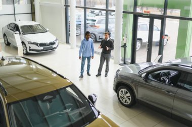 Erkek araba satıcısı araba galerisinde müşteriye araba seçmesinde yardımcı olur. Adam yeni araba alıyor..