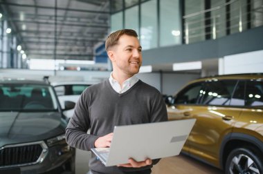 Araba satıcısı araba salonunda duruyor ve müşterilerin satışa çıkmasını bekliyor..