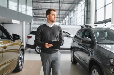 Araba satıcısı araba salonunda duruyor ve müşterilerin satışa çıkmasını bekliyor..