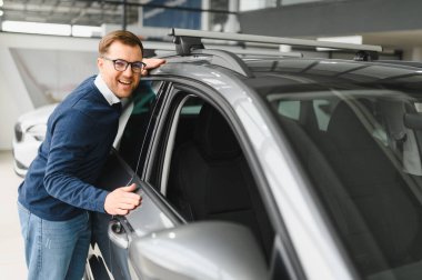 Genç adam yeni bir araç içinde araba Bayilik seçmektir.