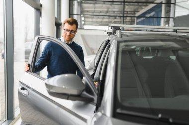 Bugün yeni bir araba aldım. Yerel bayilikte yeni arabasının yanında poz veren mutlu, olgun bir adamın portresi..