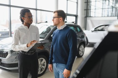 Erkek araba satıcısı, galeride dalgın genç bir müşteriyle sohbet ediyor. Satış merkezinden araba alırken adam dinliyor.