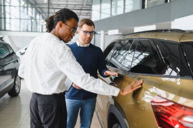 Erkek müşterinin portresi galeride profesyonel araba satıcısıyla konuşuyor. Yeni otomobil seçimi ve satın alma kavramı.