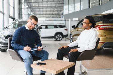 Müşteri erkek, galeride otomobil satın alıyor, araba satıcısıyla kağıt imzalıyor. Galeride yeni otomobil alma kavramı.