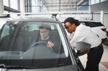 Erkek müşterinin portresi galeride profesyonel araba satıcısıyla konuşuyor. Yeni otomobil seçimi ve satın alma kavramı.