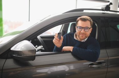 Genç adam yeni bir araç içinde araba Bayilik seçmektir.