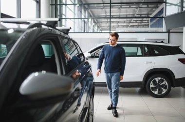 Genç adam yeni bir araç içinde araba Bayilik seçmektir.