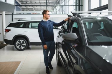 Genç yakışıklı bir adam araba galerisinde araba seçiyor..