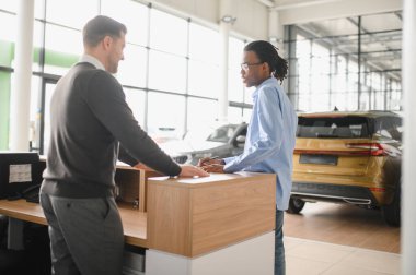 Müşteri erkek, galeride otomobil satın alıyor, araba satıcısıyla kağıt imzalıyor. Galeride yeni otomobil alma kavramı.