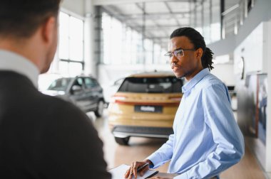 Müşteri erkek, galeride otomobil satın alıyor, araba satıcısıyla kağıt imzalıyor. Galeride yeni otomobil alma kavramı.