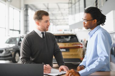 Müşteri erkek, galeride otomobil satın alıyor, araba satıcısıyla kağıt imzalıyor. Galeride yeni otomobil alma kavramı.