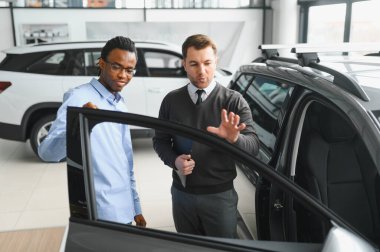 Erkek müşterinin portresi galeride profesyonel araba satıcısıyla konuşuyor. Yeni otomobil seçimi ve satın alma kavramı.