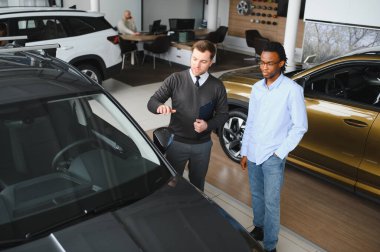 Erkek müşterinin portresi galeride profesyonel araba satıcısıyla konuşuyor. Yeni otomobil seçimi ve satın alma kavramı.