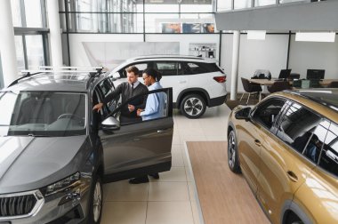 Erkek müşterinin portresi galeride profesyonel araba satıcısıyla konuşuyor. Yeni otomobil seçimi ve satın alma kavramı.