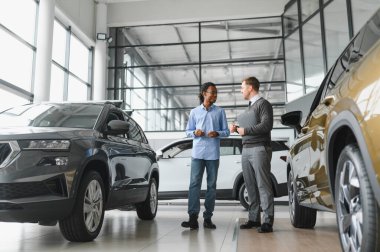 Erkek müşterinin portresi galeride profesyonel araba satıcısıyla konuşuyor. Yeni otomobil seçimi ve satın alma kavramı.