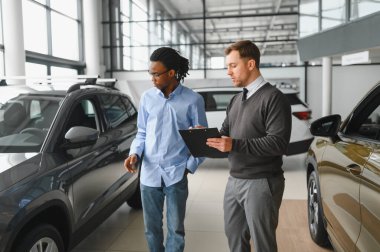 Erkek araba satıcısı, galeride dalgın genç bir müşteriyle sohbet ediyor. Satış merkezinden araba alırken adam dinliyor.