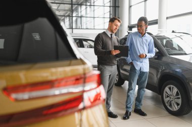 Erkek araba satıcısı araba galerisinde müşteriye araba seçmesinde yardımcı olur. Adam yeni araba alıyor..