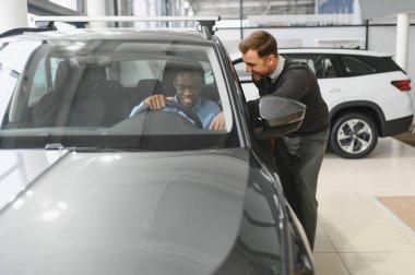Erkek araba satıcısı araba galerisinde müşteriye araba seçmesinde yardımcı olur. Adam yeni araba alıyor..