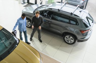 Erkek araba satıcısı araba galerisinde müşteriye araba seçmesinde yardımcı olur. Adam yeni araba alıyor..