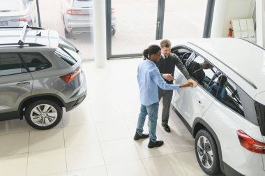 Erkek araba satıcısı araba galerisinde müşteriye araba seçmesinde yardımcı olur. Adam yeni araba alıyor..