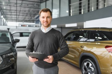 Araba satıcısı araba salonunda duruyor ve müşterilerin satışa çıkmasını bekliyor..