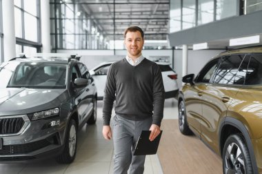 Araba satıcısı araba salonunda duruyor ve müşterilerin satışa çıkmasını bekliyor..