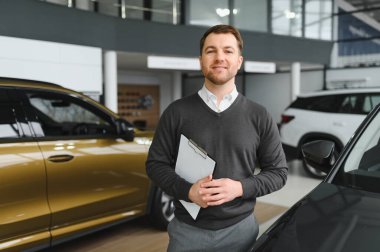 Araba satıcısı araba salonunda duruyor ve müşterilerin satışa çıkmasını bekliyor..