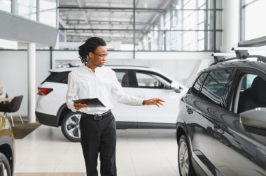 Afrikalı araba satıcısı araba galerisinde duruyor ve müşterilerin satışa çıkmasını bekliyor..