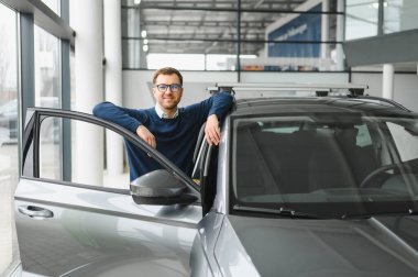 Genç adam yeni bir araç içinde araba Bayilik seçmektir.